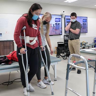 a masked patient takes steps during a physical therapy session 